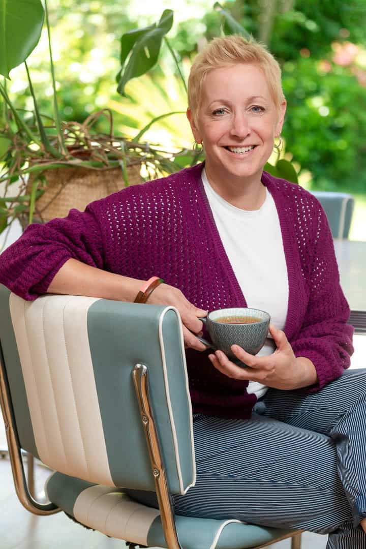 Jo Farr wearing berry cardigan holding a mug